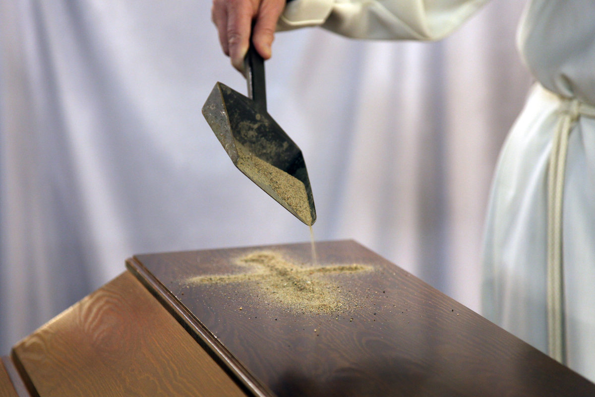 Pappi tekee hiekasta ristinmerkin arkun päälle.