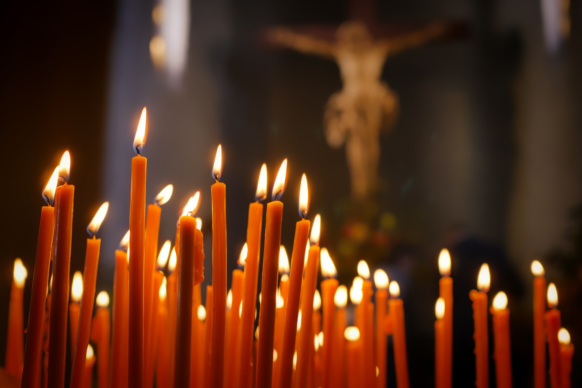 Palavat kynttilät loistavat pimeässä, taustalla Jeesus ristillä.