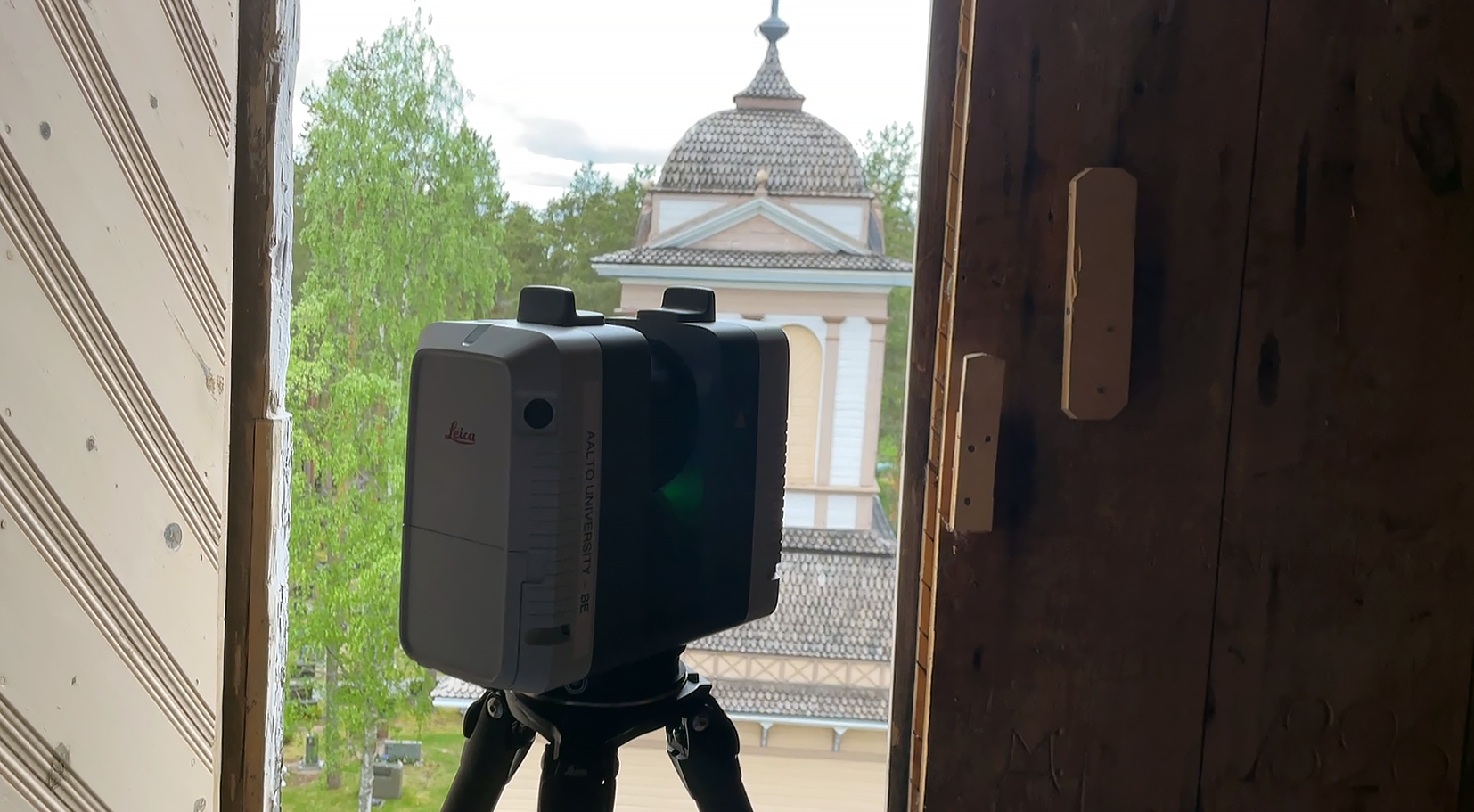 Laserkeilain jalustalla kirkon tornin avoinna olevan luukun suulla.